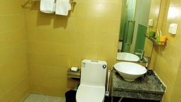 Un baño con inodoro, lavamanos y espejo. Hay toallas en un perchero sobre el inodoro.