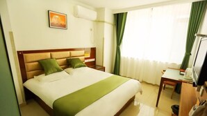 Habitación de hotel con cama, escritorio, silla, televisión y ventana con cortinas.