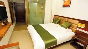Habitación de hotel con cama, televisor, mesita de noche de madera y puerta corrediza de vidrio que da a un baño.