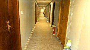 Pasillo de hotel con pisos alfombrados, puertas de madera y una botella de agua a la derecha.