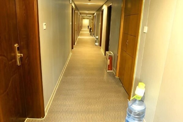 Un couloir d’hôtel avec des revêtements de sol en moquette, des portes en bois et une bouteille d’eau sur la droite.