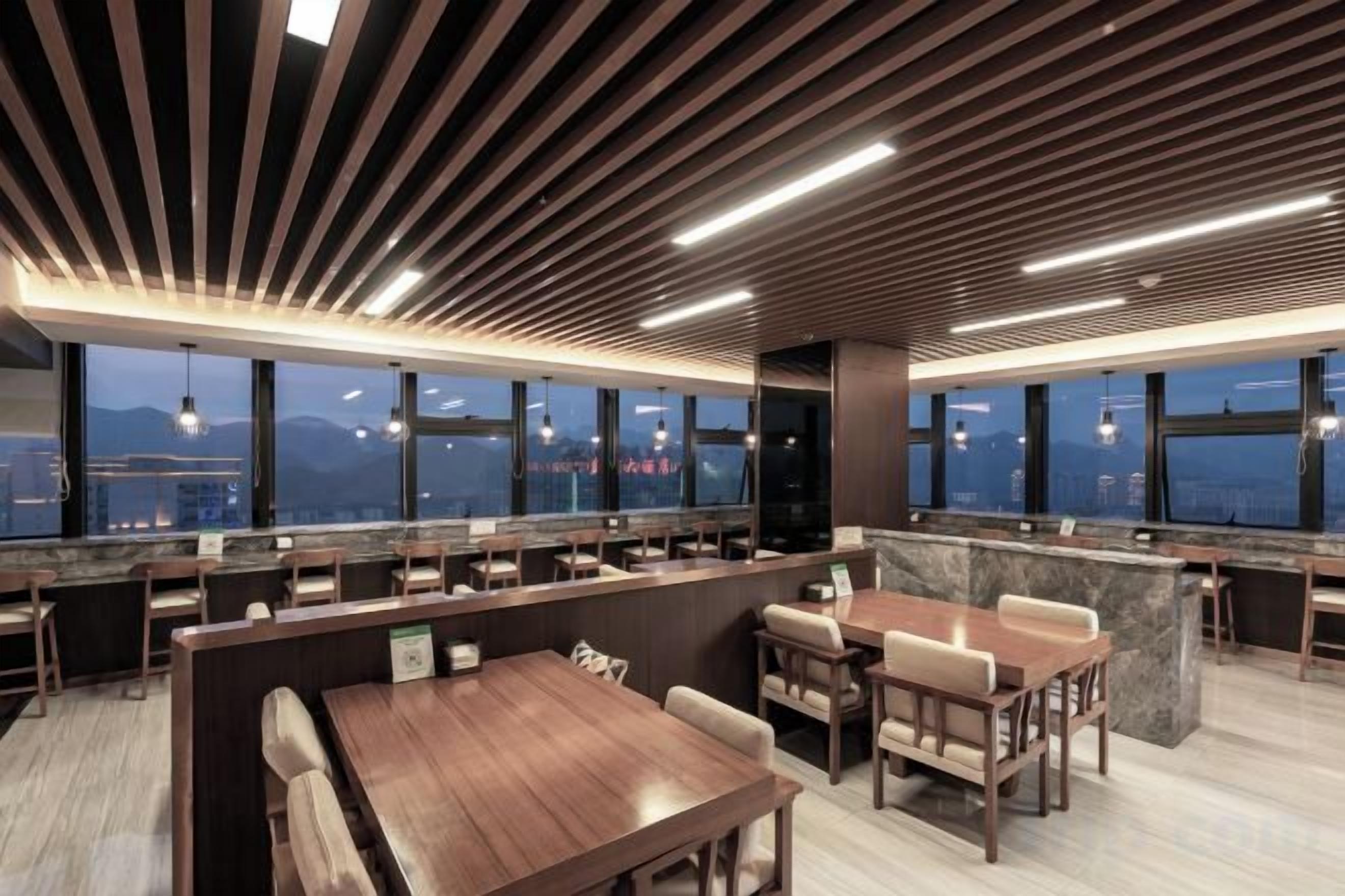 A modern restaurant with high ceilings, wooden slats, and a view of the cityscape.