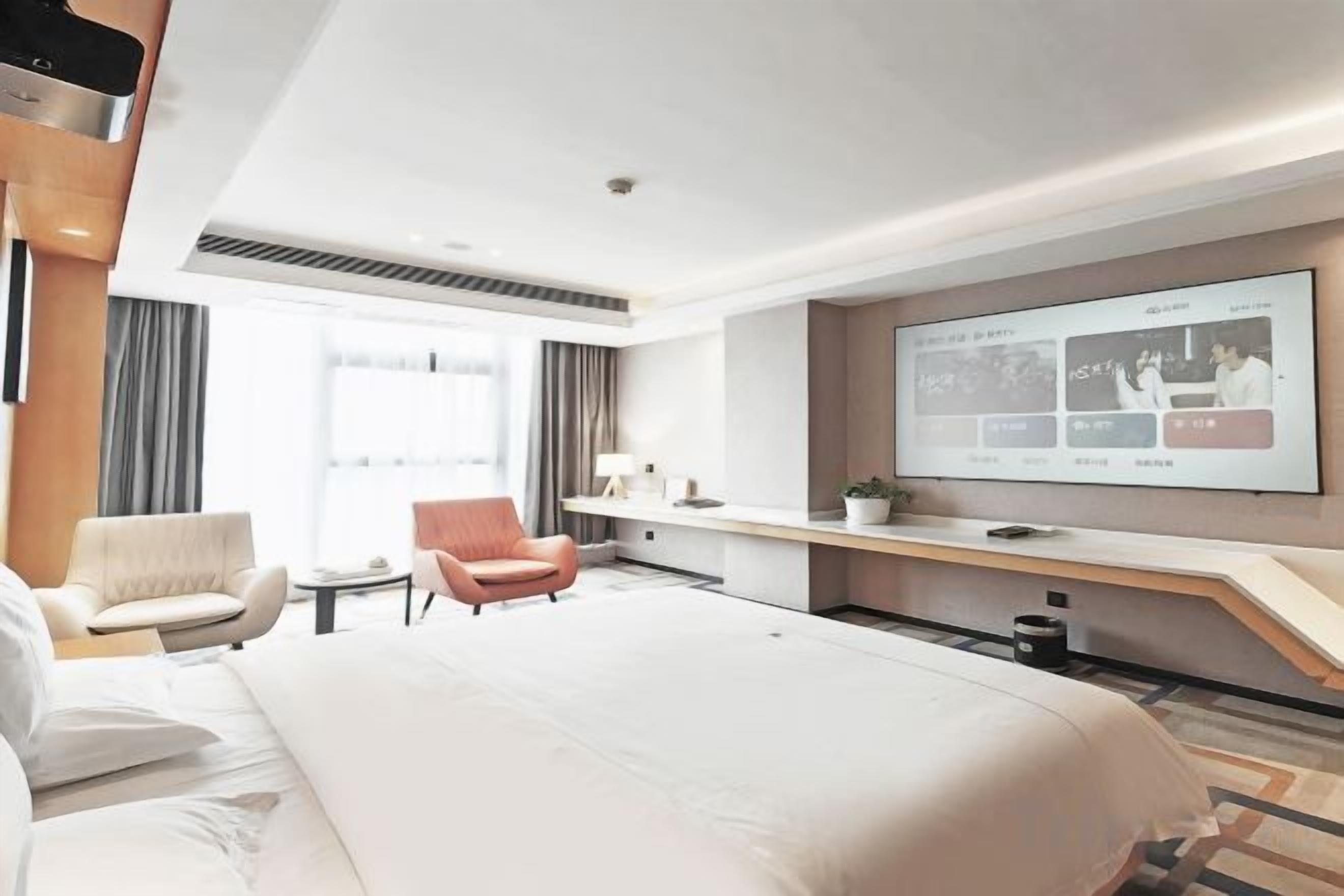 A hotel room with a large bed, a desk, a chair, a TV screen, and a window.
