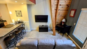 A compact living space with a sofa, a dining area with chairs, a TV mounted on the wall, and a wooden accent wall. - Park Ave Condo #3, Sauna+Hot Tub (Park City)