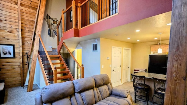 A spacious living area with a wooden staircase, a sofa, a dining table with chairs, and a kitchen area with a refrigerator. - Park Ave Condo #3, Sauna+Hot Tub (Park City)
