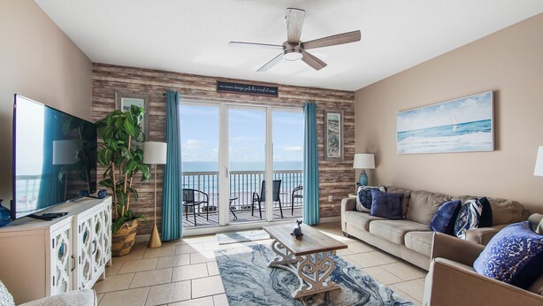 A living room with a TV, a sofa, a coffee table, and a view of the ocean through a sliding door. - Sunsets on the Gulf!  2nd Floor unit.  Available dates 8/22 - 8/31/26 (Panama City Beach)