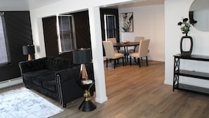 A modern living room with a black sofa, a coffee table, and a dining area with a table and chairs.