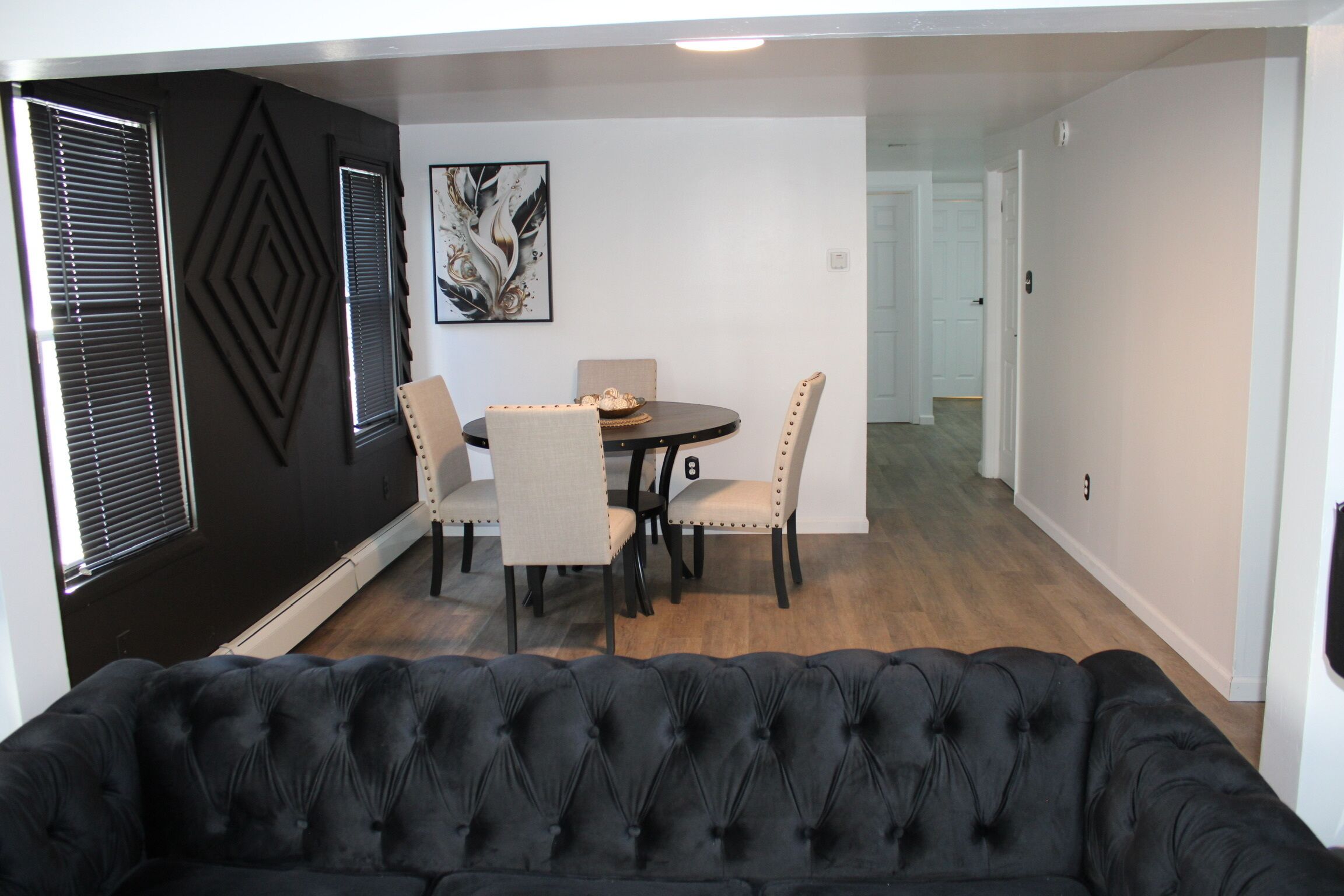 A dining area with a round table, four chairs, and a black sofa in the foreground.