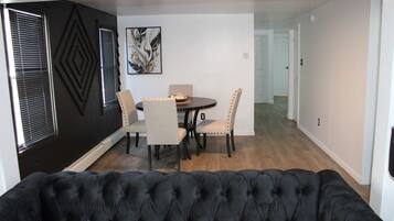 A dining area with a round table, four chairs, and a black sofa in the foreground.