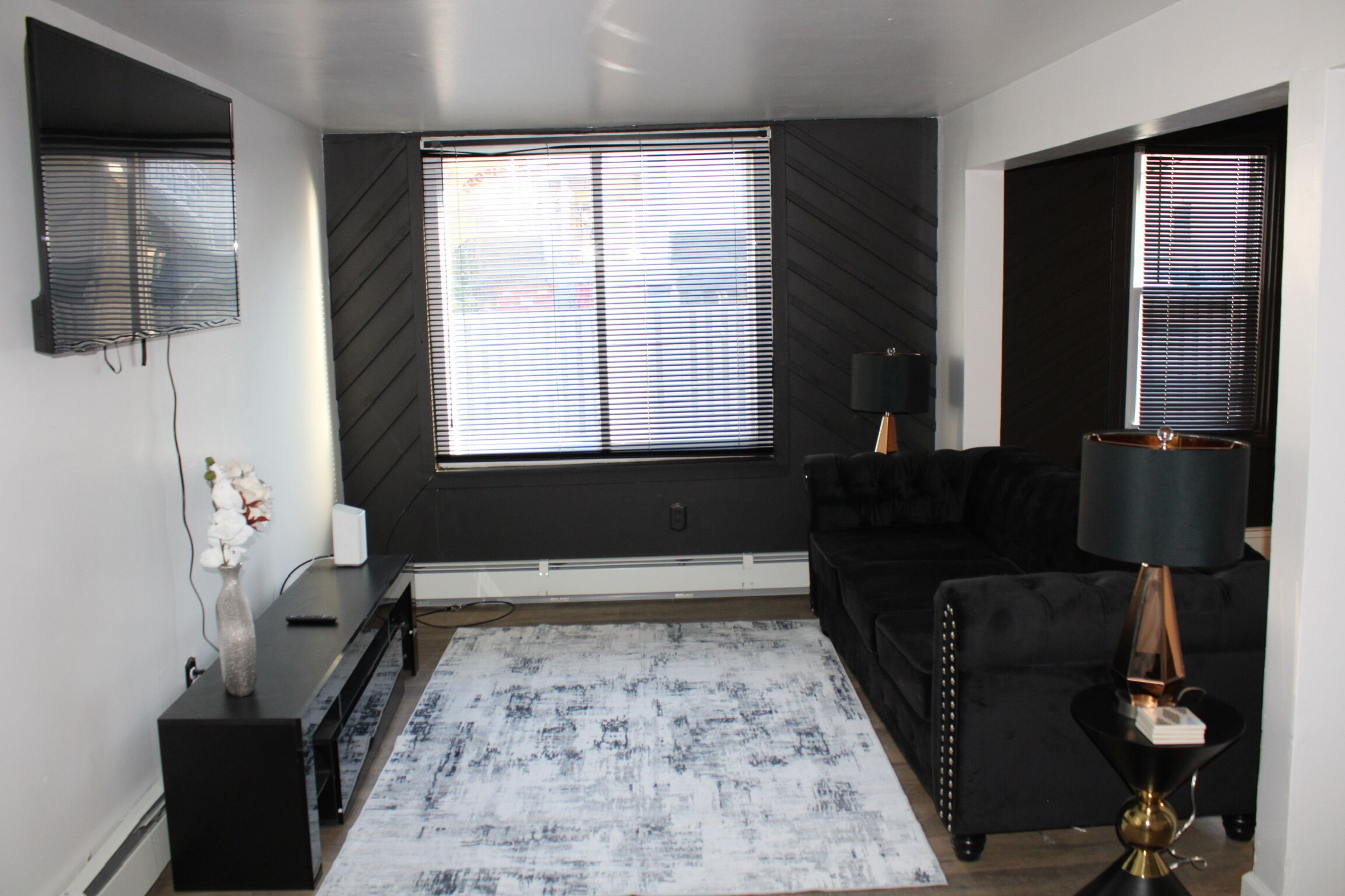 A modern living room with a large window, a black sofa, a coffee table, and a lamp.