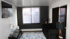A modern living room with a large window, a black sofa, a coffee table, and a lamp.
