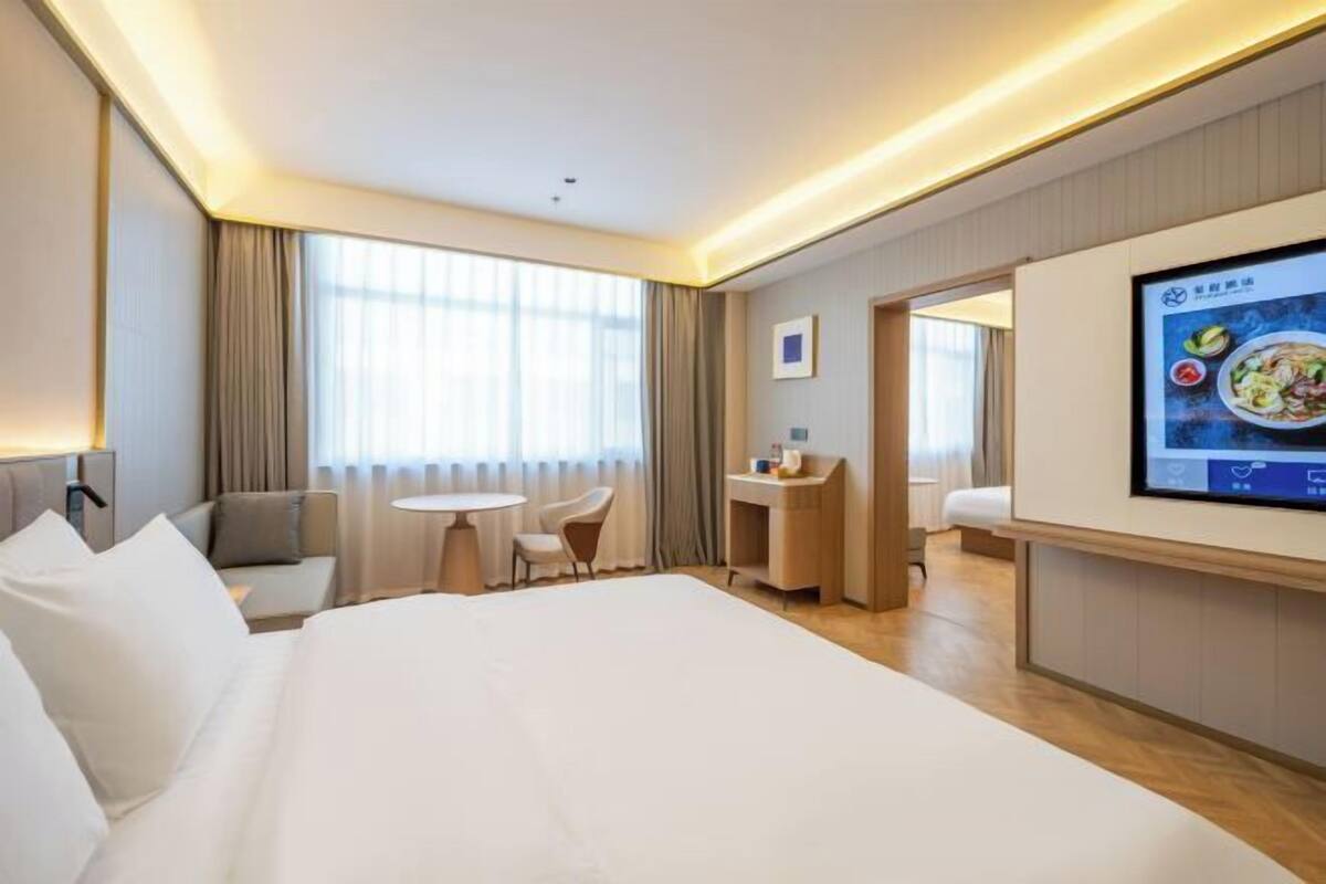 A hotel room with a large bed, a desk, a chair, a small table, and a TV on the wall.