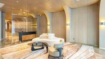 Un moderno vestíbulo de hotel con un mostrador de recepción curvo, una zona de estar con sofá y sillones, y un suelo de mármol.