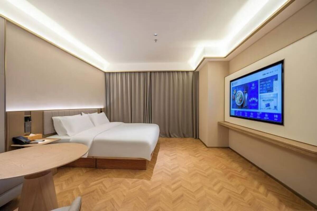 A modern hotel room with a large bed, a desk, and a flat-screen TV mounted on the wall.