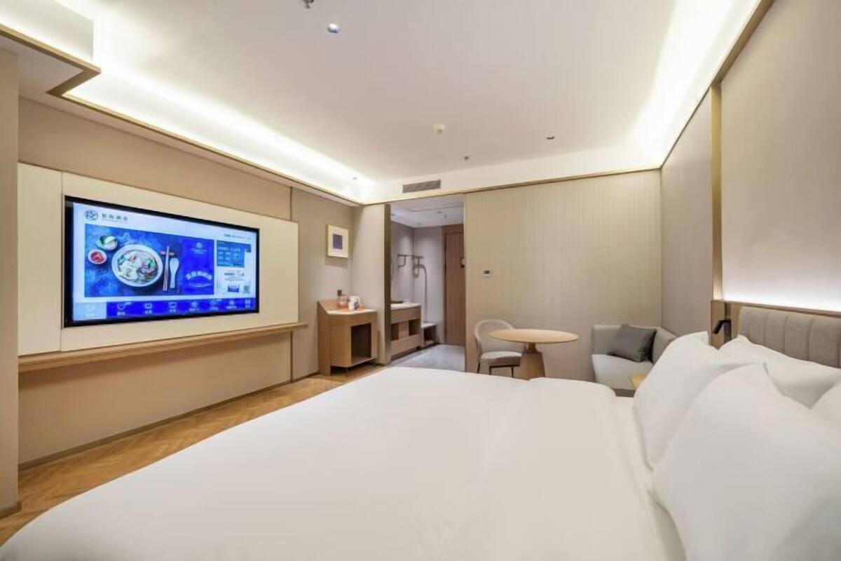 A modern hotel room with a large bed, a TV mounted on the wall, a small table, and a chair.
