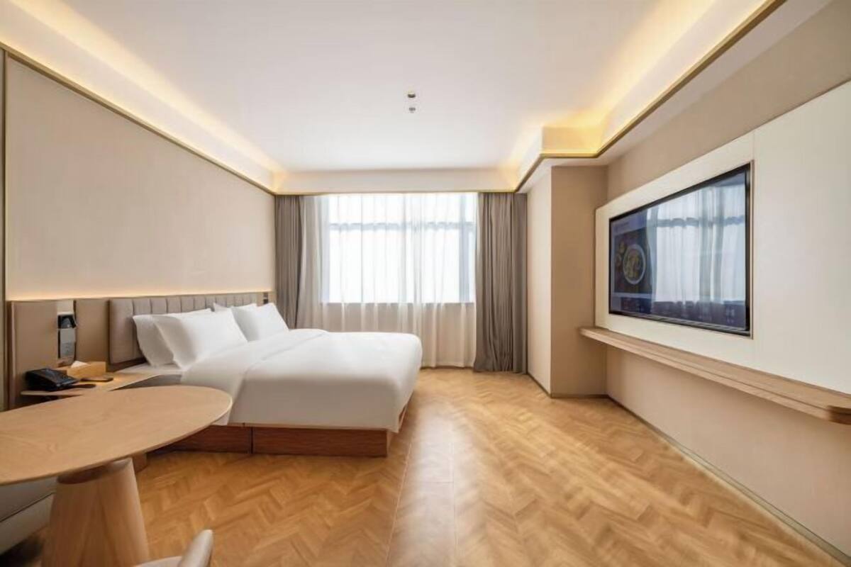 A hotel room with a bed, bedside table, lamp, and a large window with curtains.