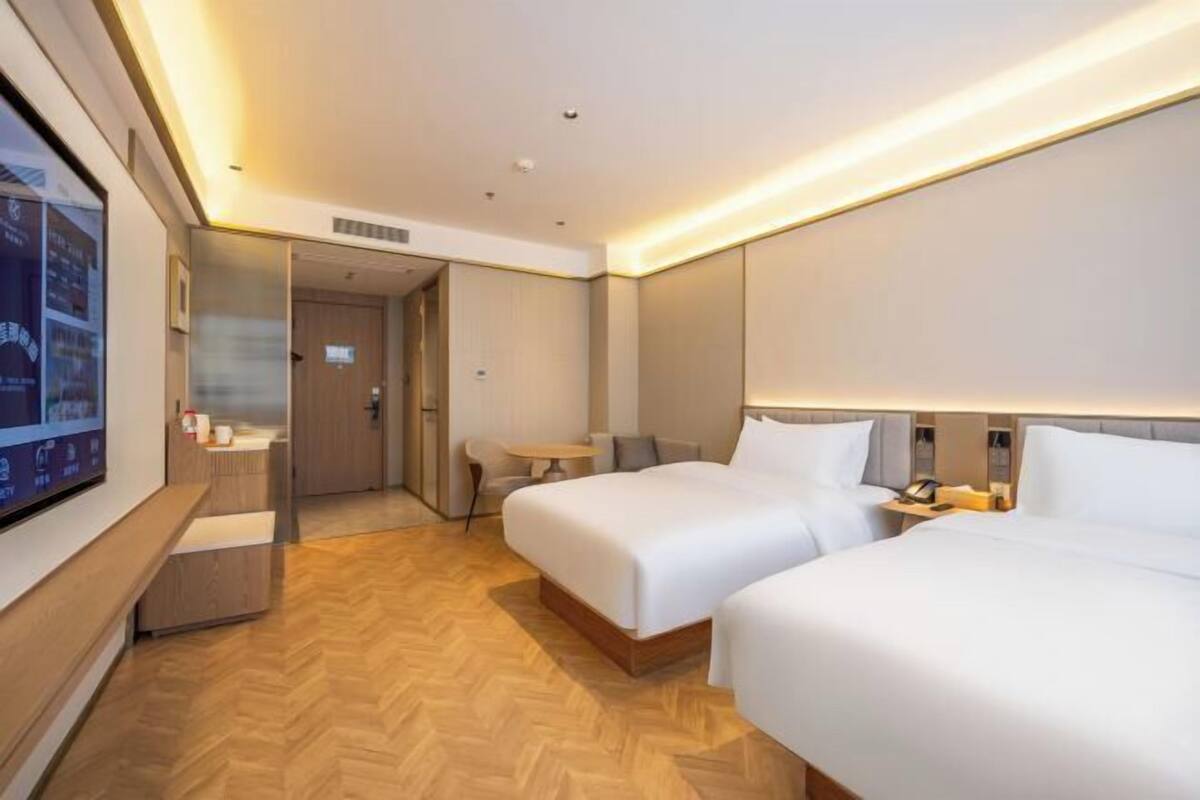 A hotel room with two beds, a desk, and a TV on the wall.