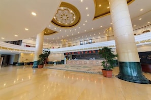 A spacious lobby with a high ceiling, large columns, and a central reception desk. - Ujimqin Hotel (West Ujimqin Banner)