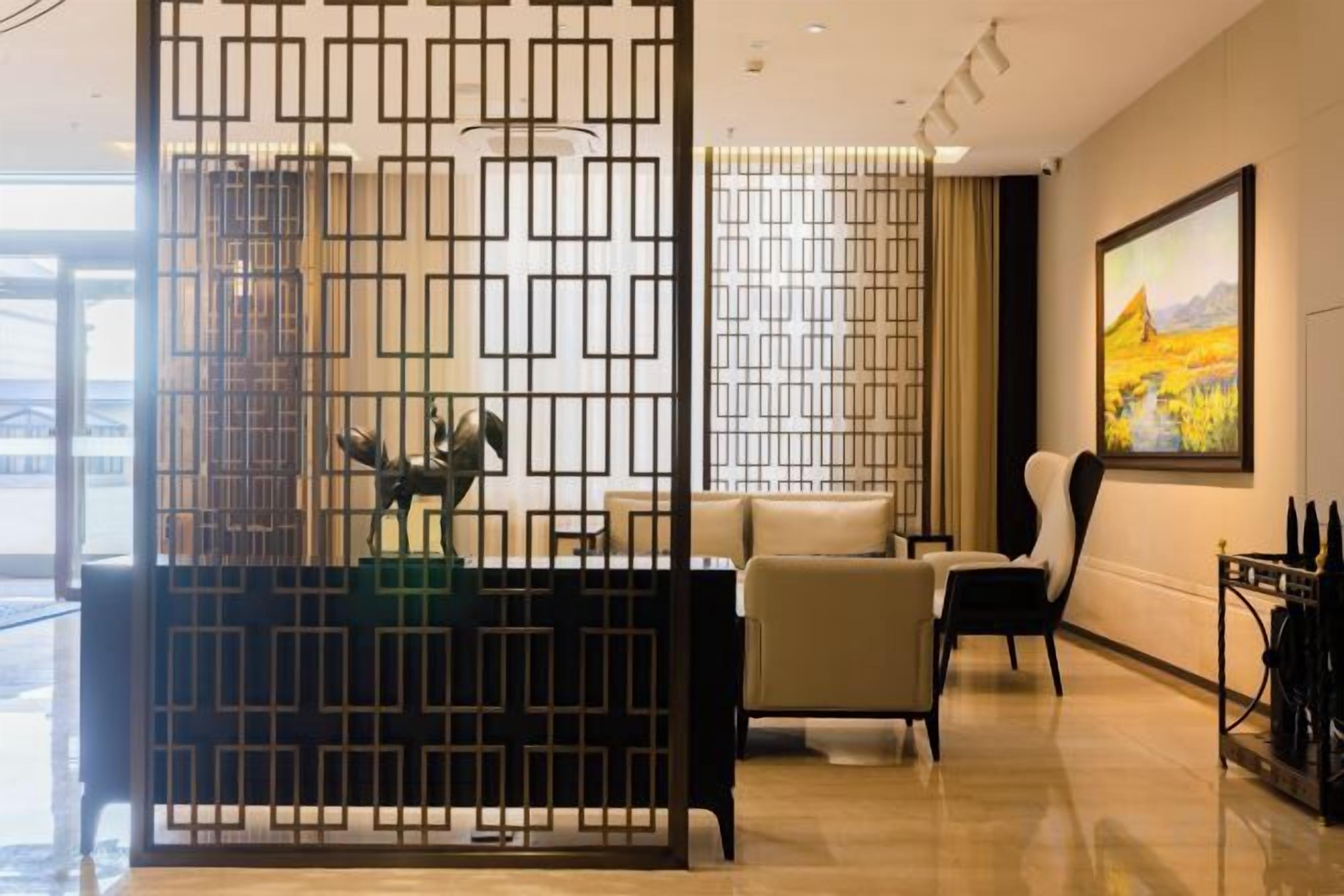 A modern hotel lobby with a reception desk, seating area, and a large painting on the wall.