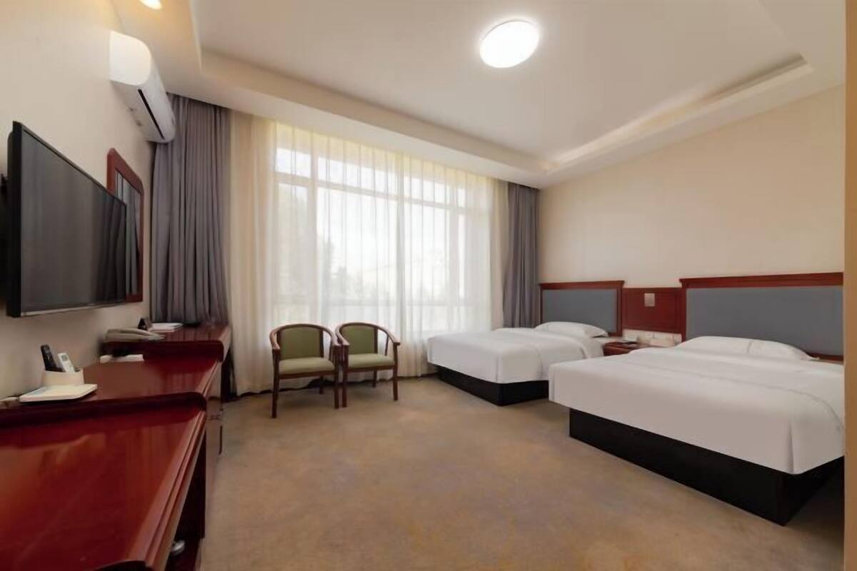 A hotel room with two beds, a desk, a chair, a TV, and a window with curtains.