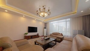 A modern living room with a large sofa set, a flat-screen TV, a chandelier, and a large window with curtains.