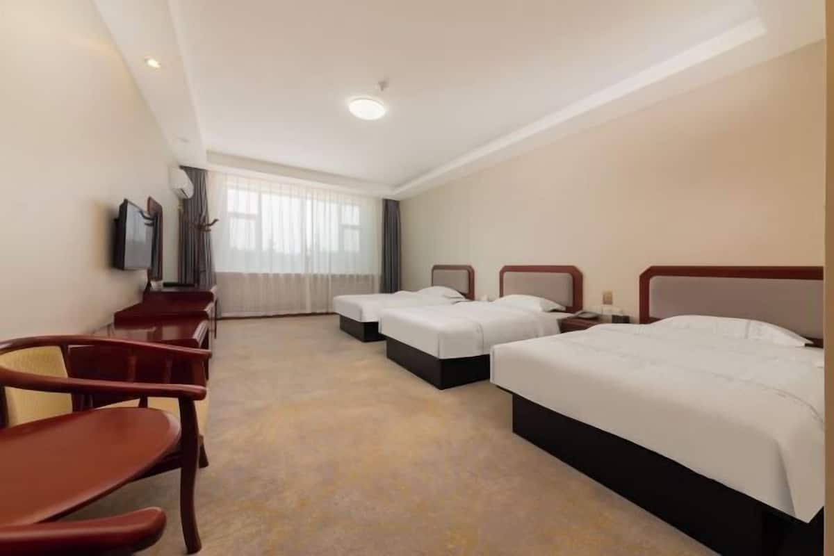 A hotel room with three beds, a TV, a desk, and a chair.