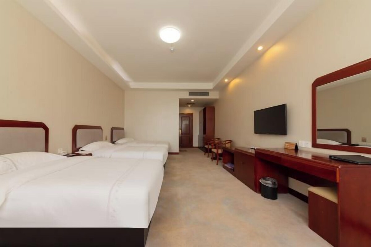 Una habitación de hotel con dos camas, un escritorio, una silla, un televisor y un espejo.
