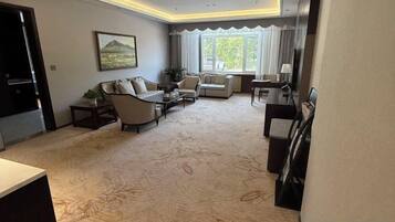 Une chambre d’hôtel comprenant un coin salon, un canapé, une table basse, une télévision et une fenêtre avec des rideaux.