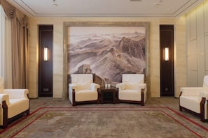 A room with a large wall mural, two armchairs, a small table, and a carpeted floor. - Ujimqin Hotel (West Ujimqin Banner)