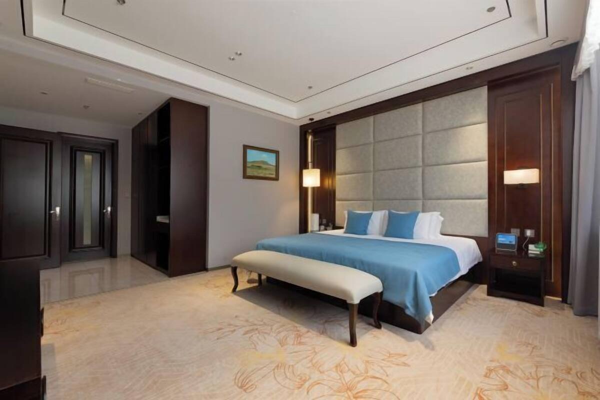 A hotel room with a large bed, a bench, a nightstand, and a door.