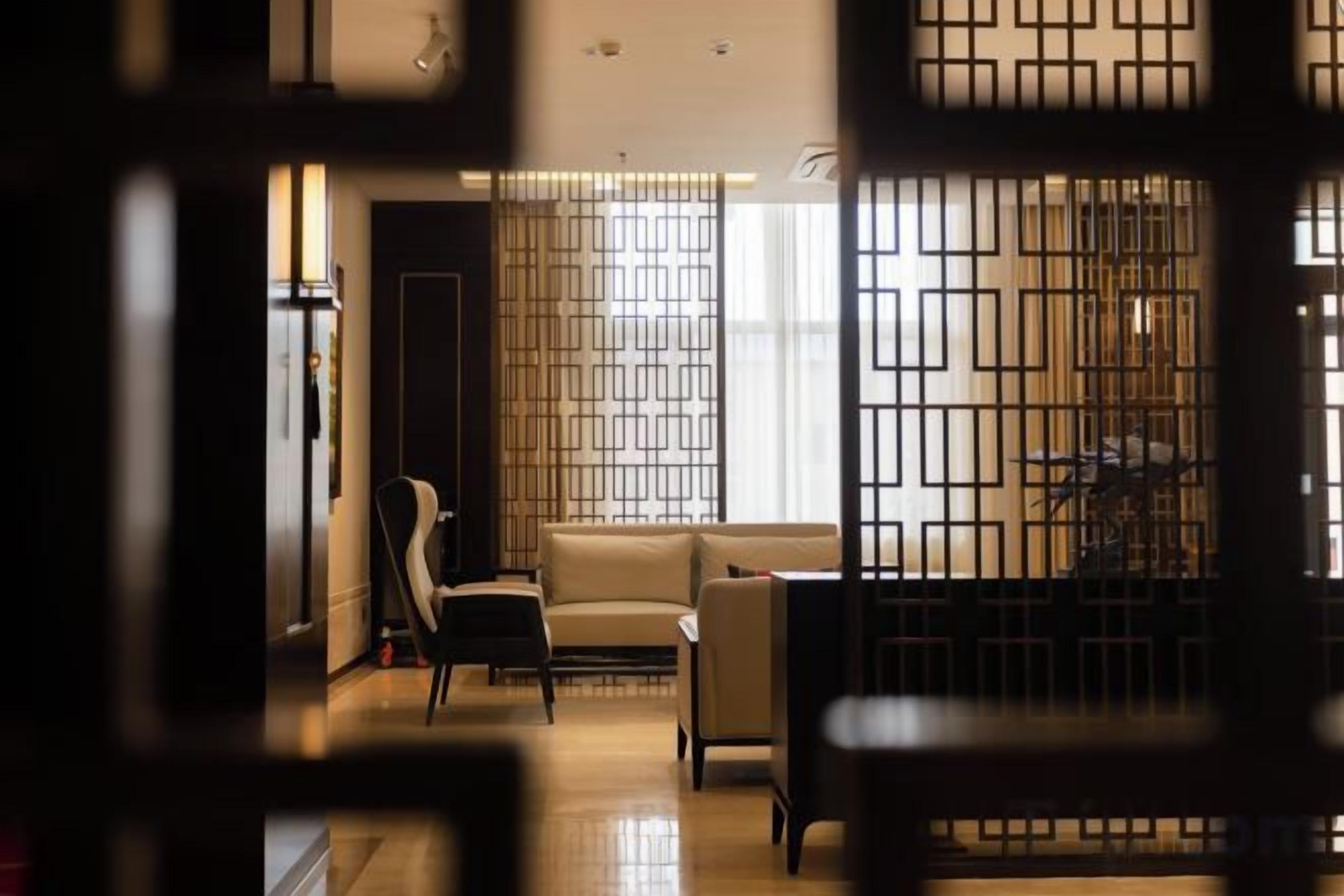 A room with a sofa, chairs, and a table. There is a partition with a geometric pattern.