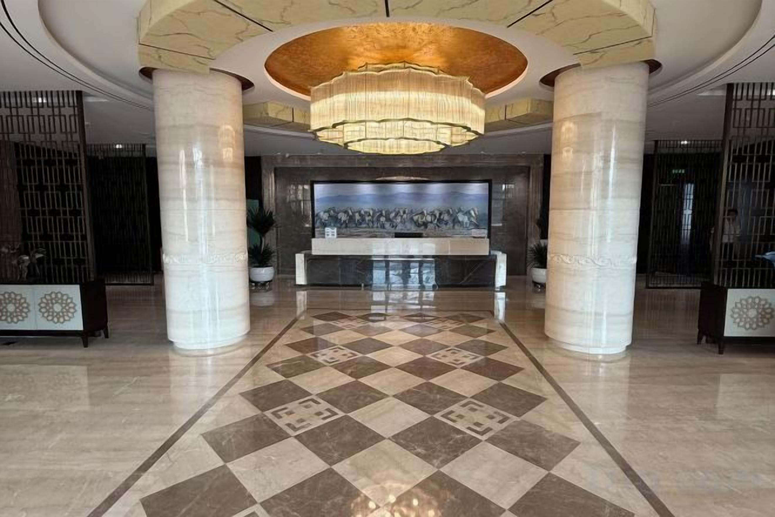 A lobby with a checkered floor, a reception desk, and a large chandelier.