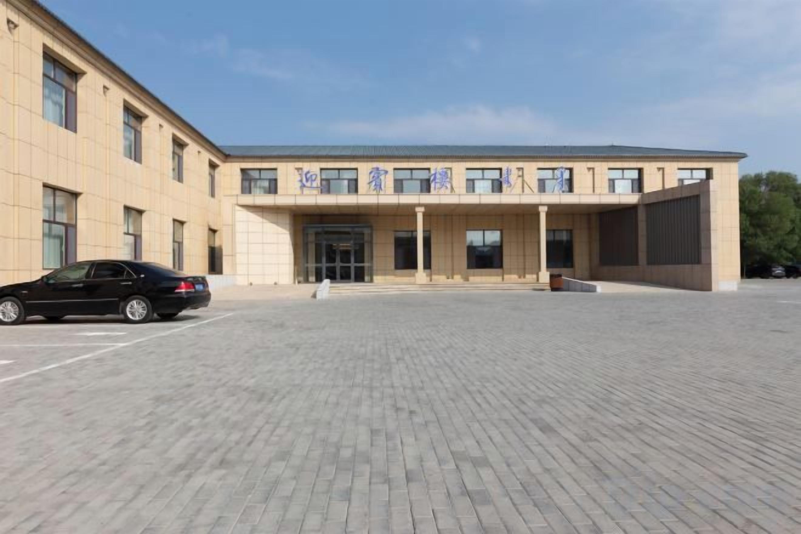 A modern building with a paved entrance area and a black car parked in front.