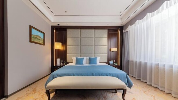 A modern hotel room with a large bed, a headboard with a tufted design, and a view of a landscape through sheer curtains.