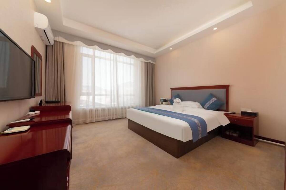 A hotel room with a bed, a desk, a TV, and a window with curtains.