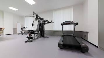 Un gimnasio con cinta de correr, máquinas de pesas y un banco.