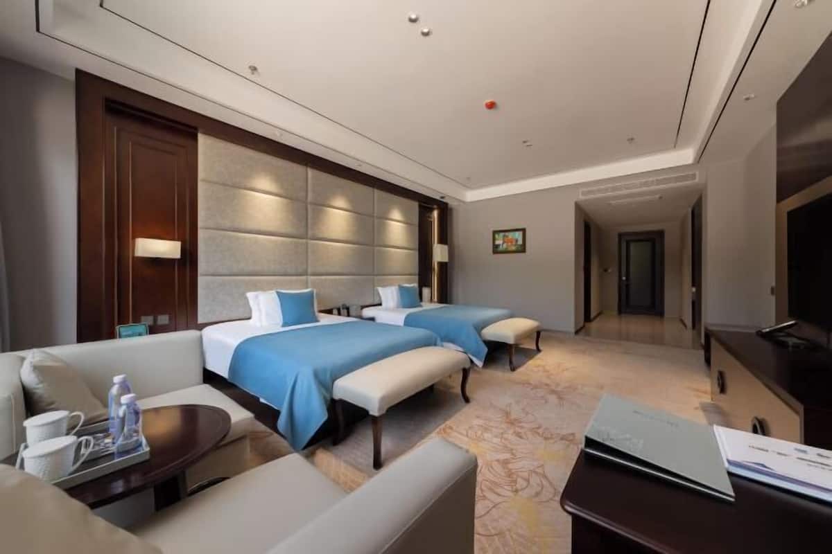 A hotel room with two beds, a sofa, a TV, and a desk with a laptop.