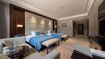A hotel room with two beds, a sofa, a TV, and a desk with a laptop.