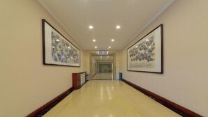 A hotel corridor with framed artwork on the walls, a polished floor, and a ceiling with recessed lighting.
