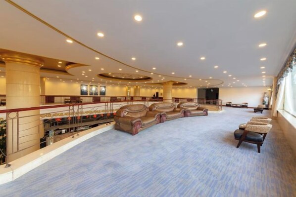 A spacious hotel lobby with a curved seating area, a balcony, and a large window providing natural light. - Ujimqin Hotel (West Ujimqin Banner)