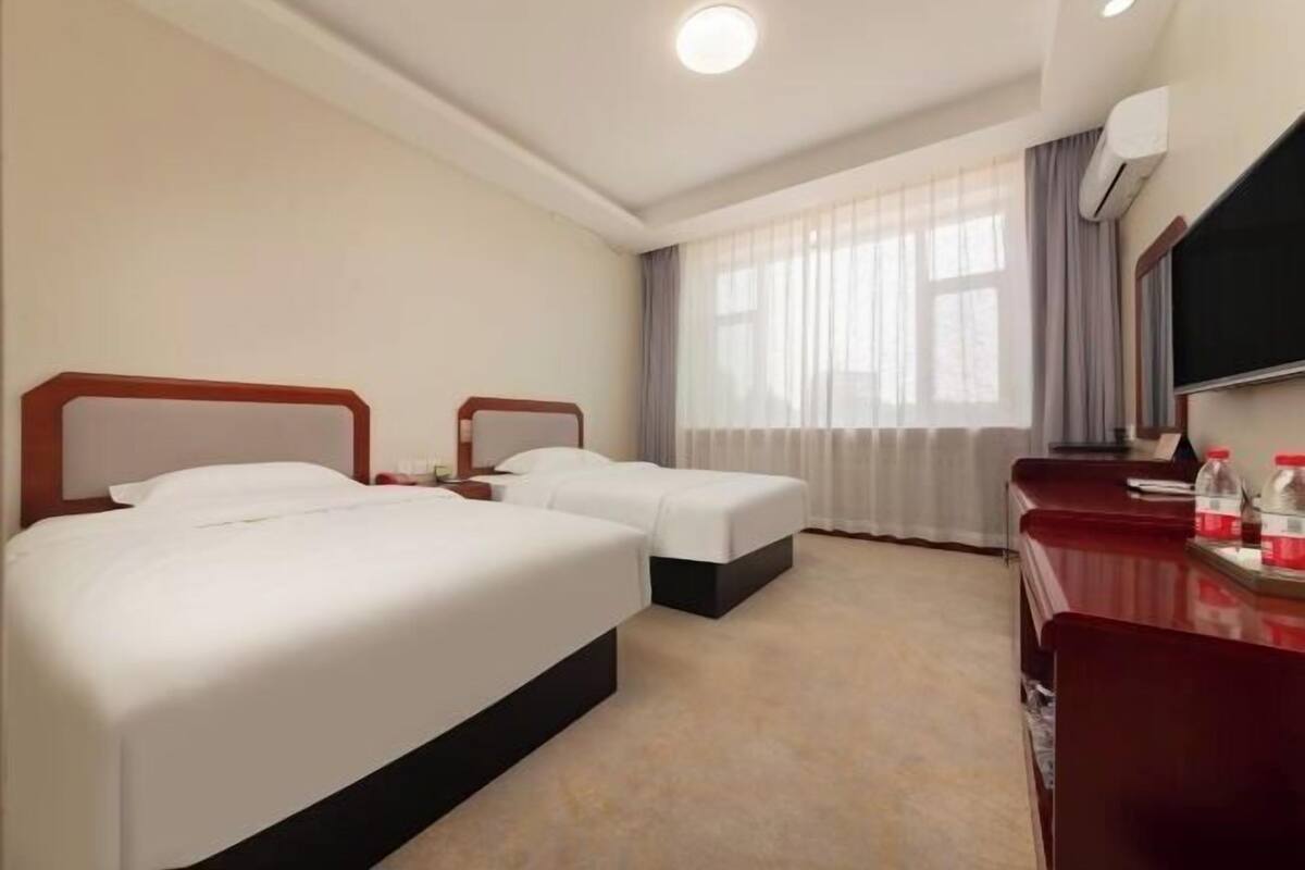 A hotel room with two beds, a desk, a TV, and a window with curtains.