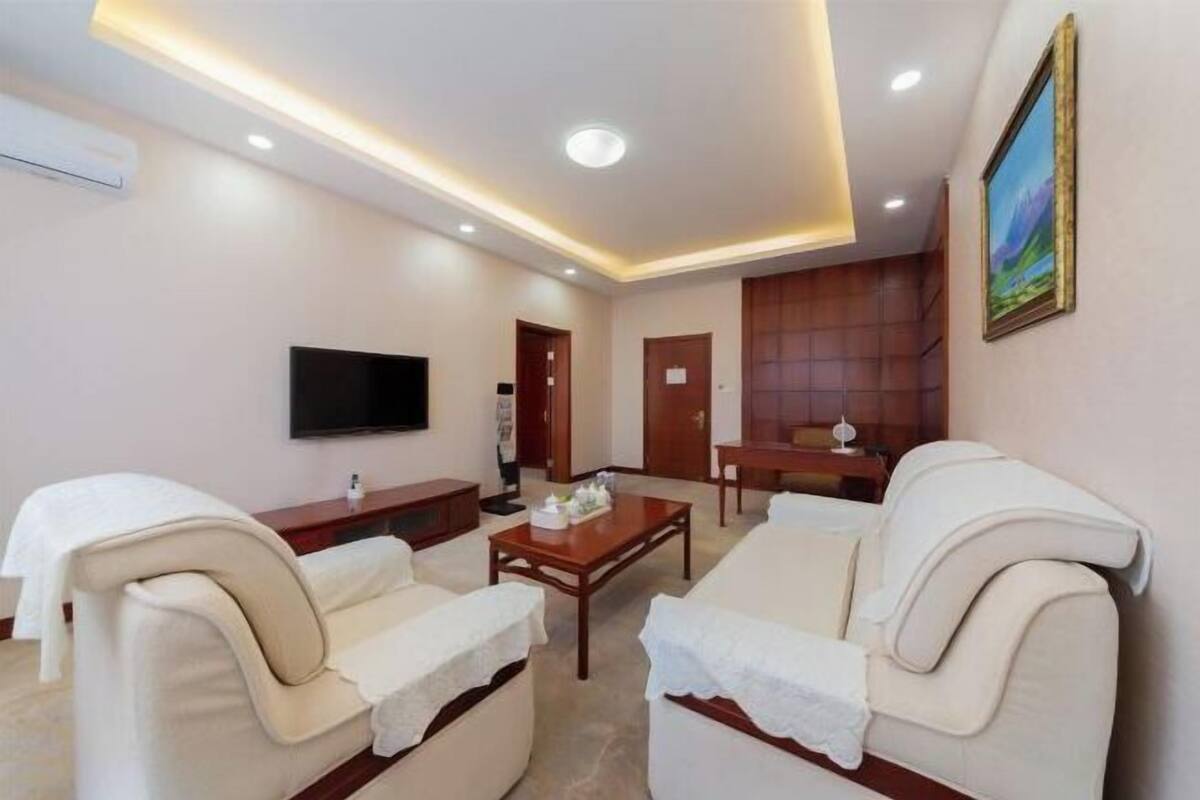 A modern living room with a flat-screen TV, beige sofas, a wooden coffee table, and recessed ceiling lighting.