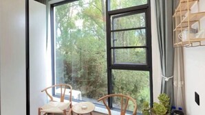 A room with a large window, two wooden chairs, a small table, and a shelf with items. - Dali Yunpingrui Boutique Homestay (Dali City)