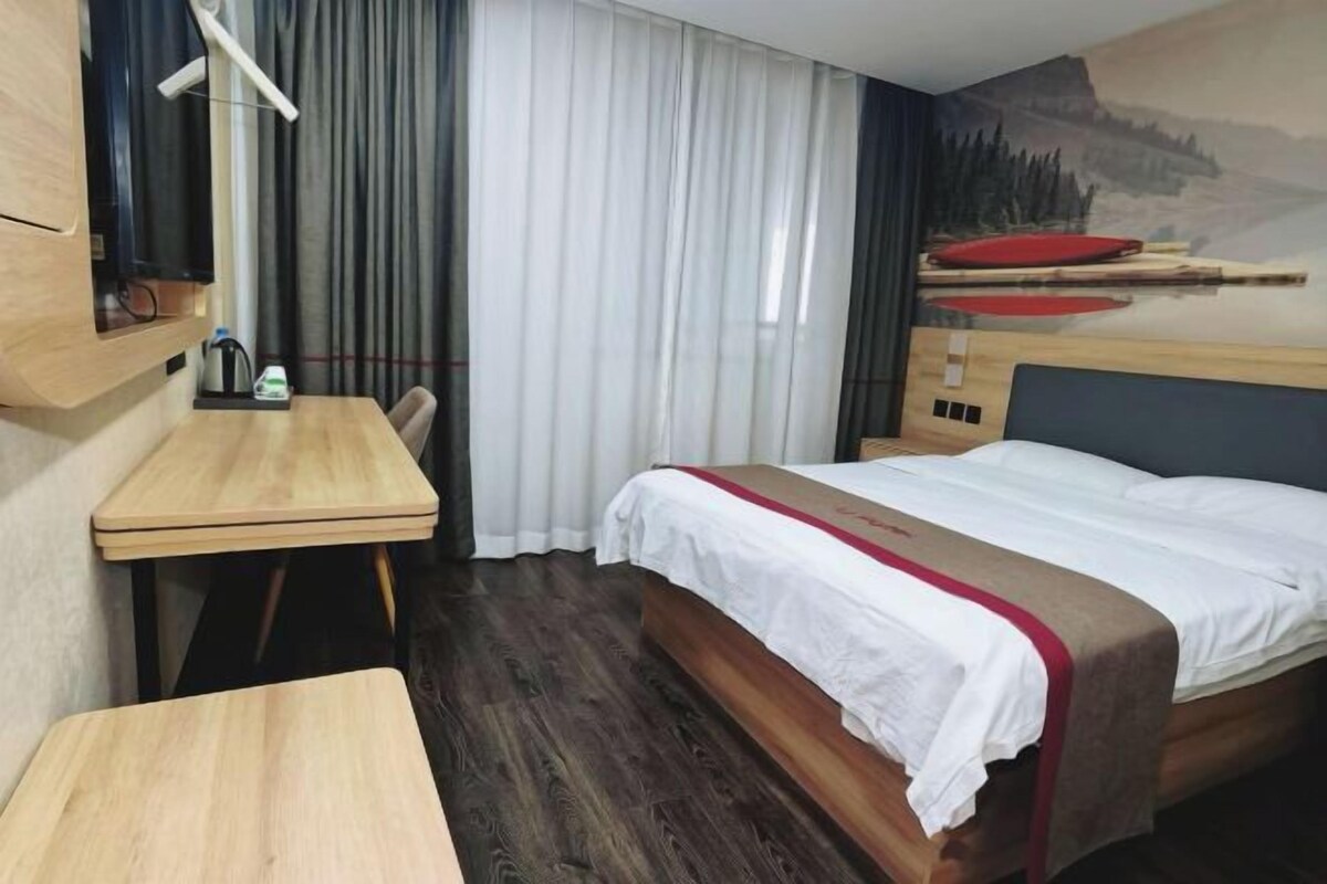 A hotel room with a bed, a desk, and a window with curtains.