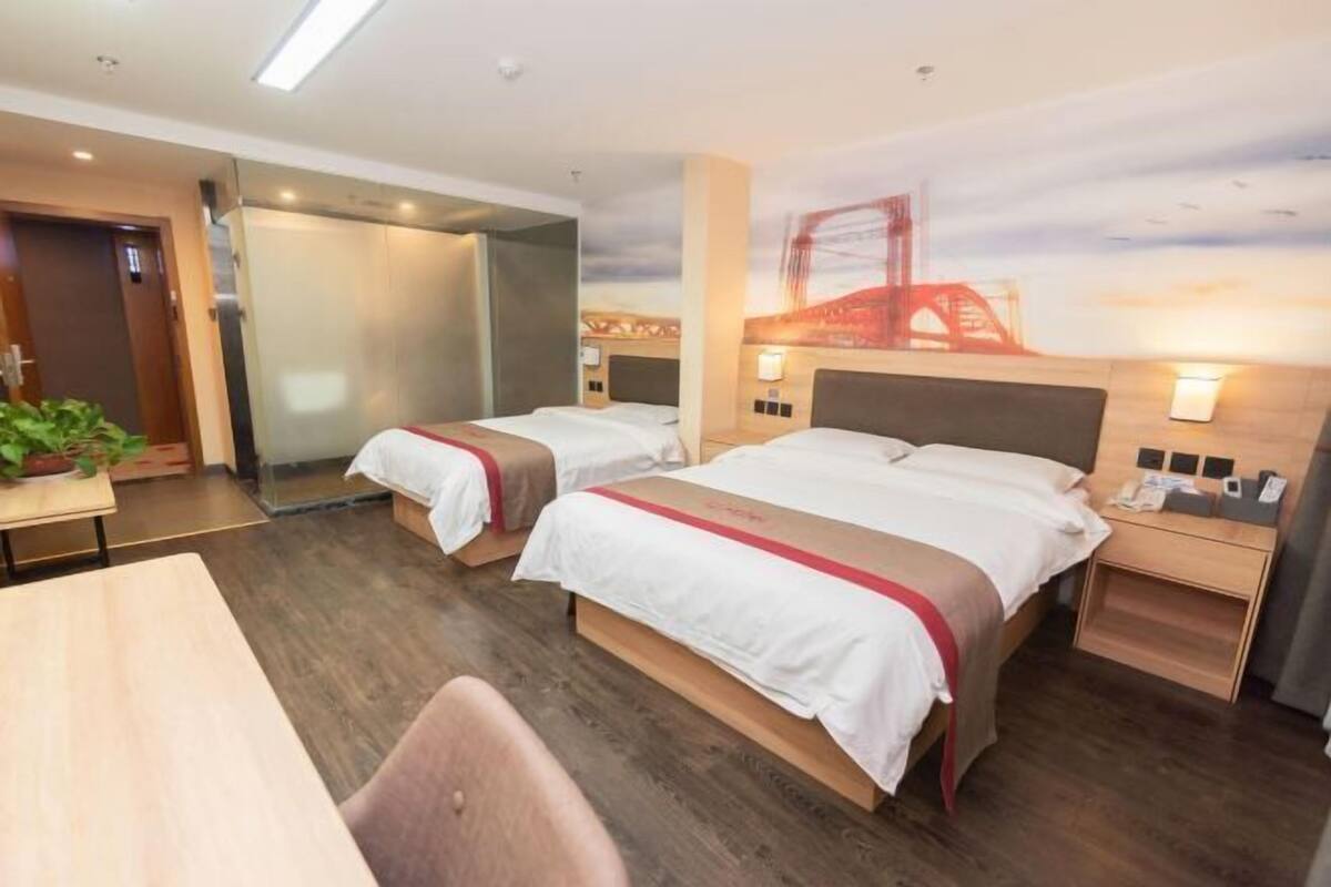 A hotel room with two beds, a desk, a chair, a nightstand, and a mural of a bridge.
