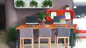Un mostrador de recepción con dos monitores de computadora, una planta y una bandeja roja con un certificado.