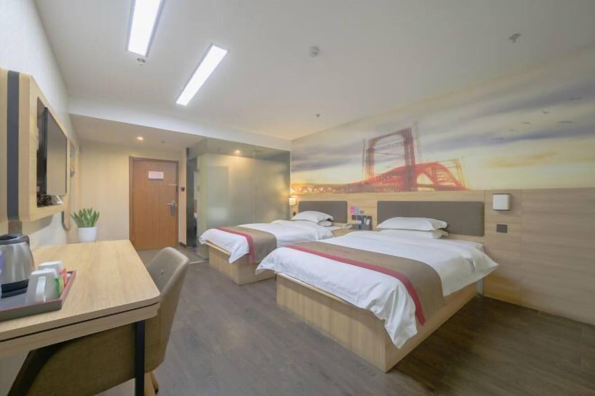 A hotel room with two beds, a desk with a coffee maker, a TV, and a mural of a bridge.