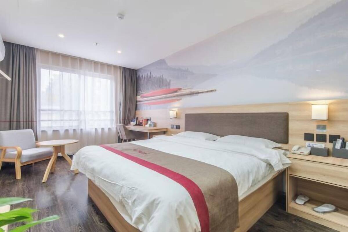 A hotel room with a bed, a desk, a chair, a small table, and a wall mural.