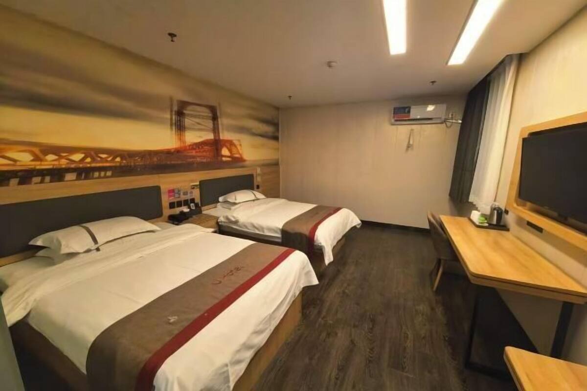 A hotel room with two beds, a desk, and a large window.