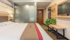 Una habitación de hotel con una cama, un televisor montado en la pared, un banco de madera y una planta en maceta.